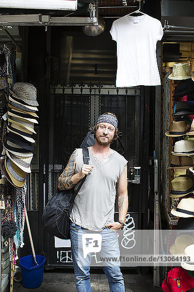 Portrait of street musician carrying guitar while standing at store