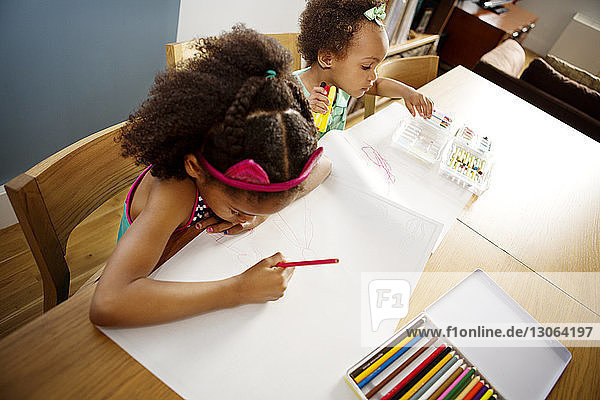 High angle view of sisters drawing on papers at table in living room