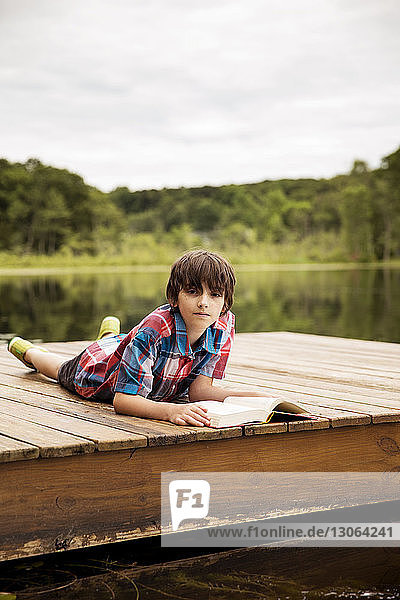 Porträt eines Jungen mit Buch  der sich auf dem Dock entspannt