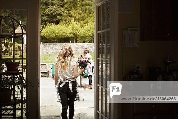 Rückansicht einer Frau  die eine Blumenvase trägt  während sie auf dem Rasen geht  durch die Tür gesehen