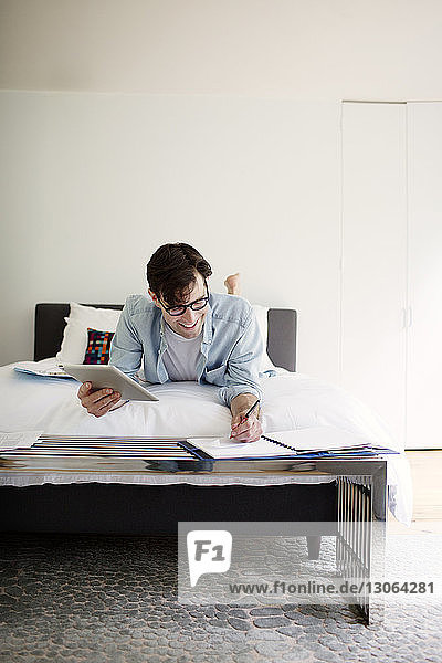 Lächelnder Mann  der einen Tablet-Computer benutzt  während er zu Hause am Bett an der Wand arbeitet