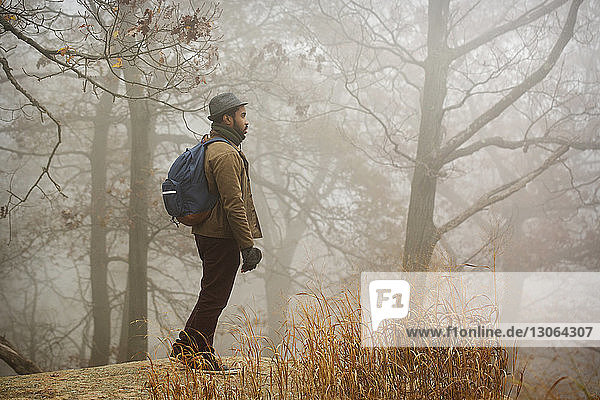 Seitenansicht eines Mannes  der wegschaut  während er auf einem Felsen im Wald steht