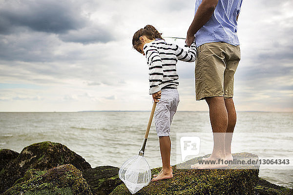 Niedriger Teil eines Mannes fischt  während er mit seiner Tochter auf einem Felsen am Meer steht