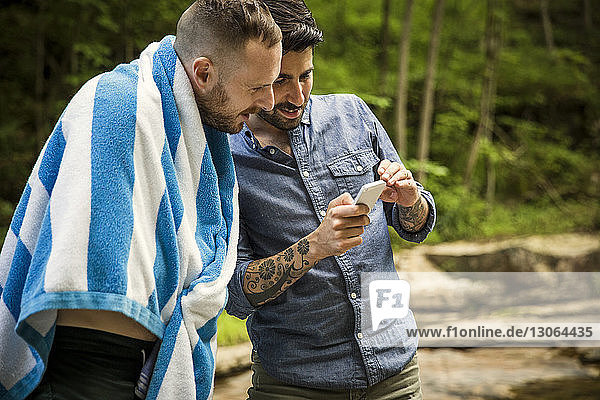 Mann zeigt seinem Freund sein Handy  während er im Wald steht