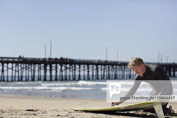 Mann bereitet sich am Strand kniend auf das Surfen vor