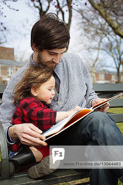 Vater und Tochter lesen Buch  während sie auf einer Parkbank sitzen