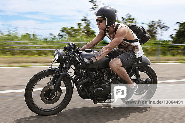 Mann mit Rucksack fährt Motorrad auf der Straße