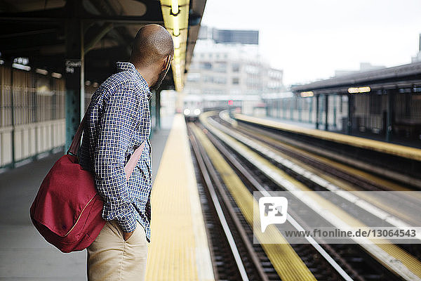 Side view of man with hand in pocket waiting for train at railroad platform