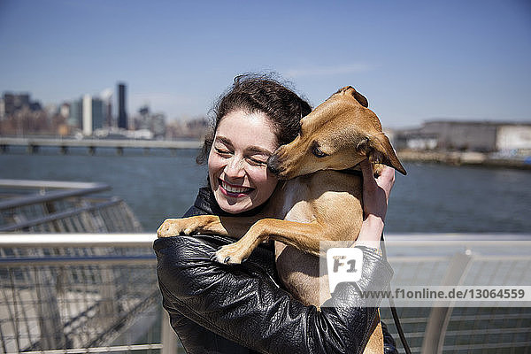 Happy woman embracing dog while standing on footbridge against sky