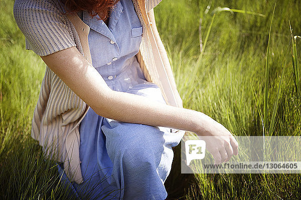 Midsection of woman crouching on grassy field