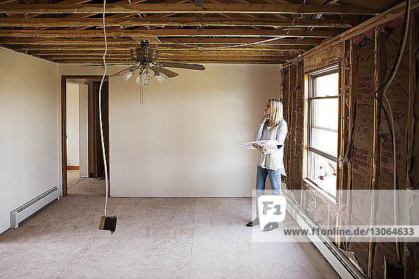 Woman with blueprint looking at fan while standing by window