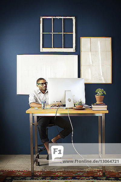 Geschäftsmann benutzt Desktop-Computer  während er im Büro am Schreibtisch sitzt