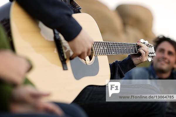 Mittendrin ein Mann  der Gitarre spielt  während er mit einem Freund zusammensitzt