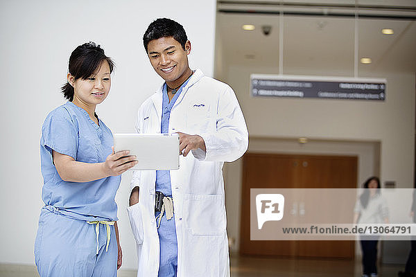 Lächelnde Ärzte schauen auf Tablet-Computer  während sie im Krankenhaus stehen
