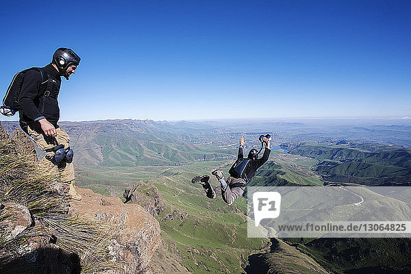 Mann sieht Freund beim Öffnen des Fallschirms an  während er auf dem Berg steht