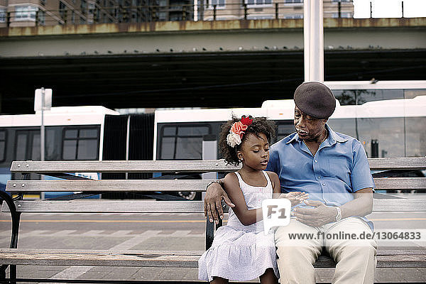 Enkelin spricht mit Großvater  während sie in der Stadt auf einer Bank sitzt