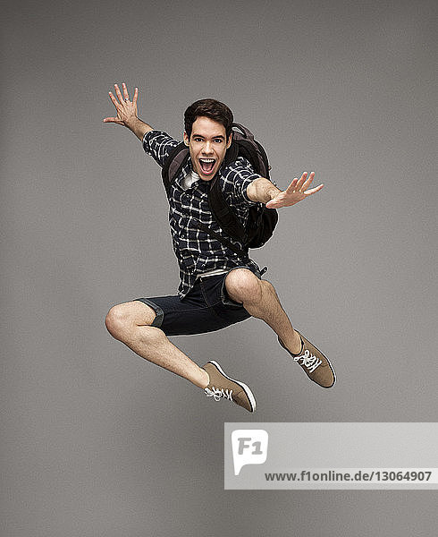 Porträt eines glücklichen Mannes mit springendem Rucksack vor grauem Hintergrund