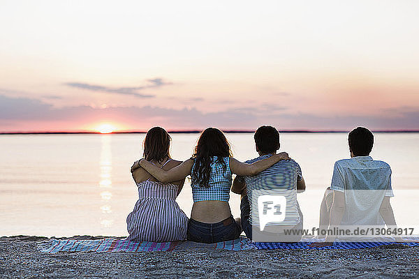 Rear view of friends relaxing at beach during sunset
