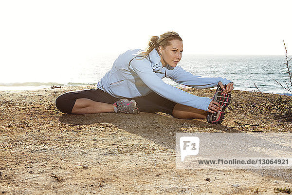 Woman touching toes while exercising at beach