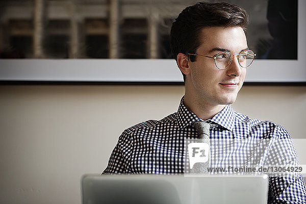 Man looking away while sitting with laptop computer at home
