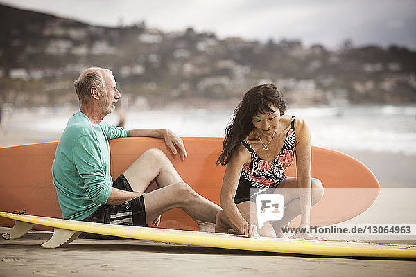 Älteres Ehepaar mit Surfbrettern am Strand sitzend