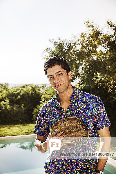 Porträt eines glücklichen Mannes mit Hut am Pool im Hinterhof
