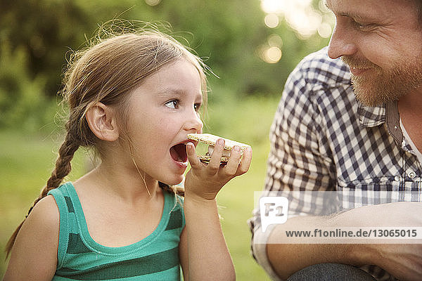 Vater sieht Tochter an  die im Sommerlager Smores isst