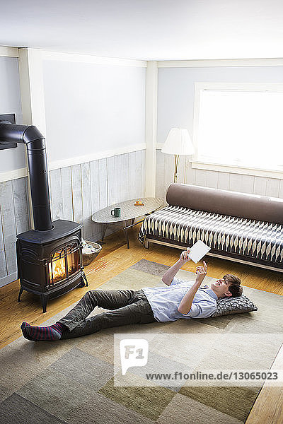 Hochwinkelansicht eines Mannes  der einen Tablet-Computer benutzt  während er zu Hause auf dem Boden liegt