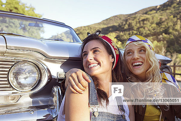 Glückliche Frauen schauen weg  während sie gegen ein Cabriolet sitzen