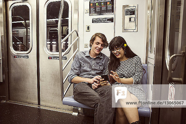 Glückliches Paar  das in der U-Bahn sitzt und auf ein Smartphone schaut