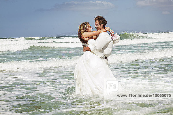 Im Meer stehendes Ehepaar am Strand gegen den Himmel