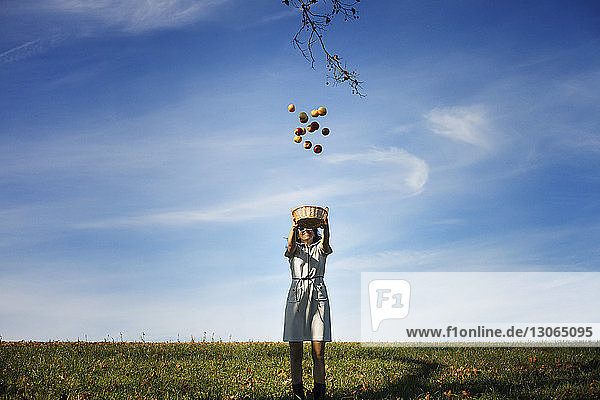Happy woman throwing apples while standing on field against sky