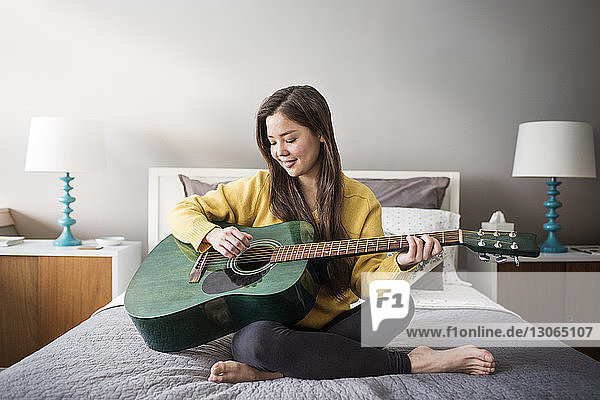 Woman playing guitar while sitting on bed at home
