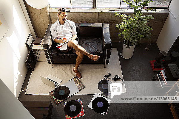 Hochwinkelansicht eines Mannes bei der Arbeit  während er zu Hause mit Aufzeichnungen und Laptop sitzt