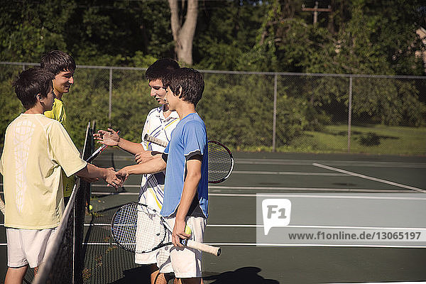 Players shaking hands over net while playing tennis at court