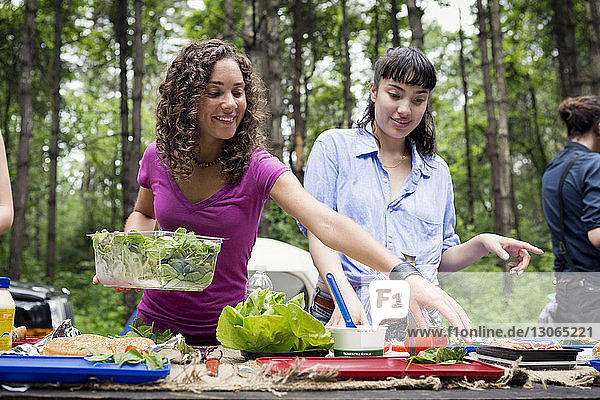 Friends arranging food at picnic table in forest