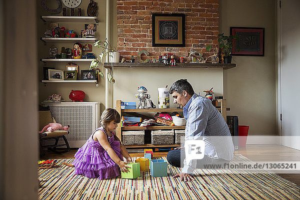 Vater schaut einem Mädchen zu  das mit Spielzeug spielt  während es zu Hause auf dem Boden sitzt