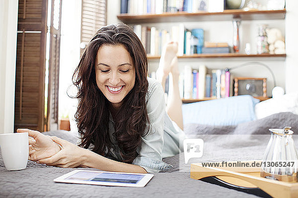 Happy woman looking at tablet computer while lying on bed