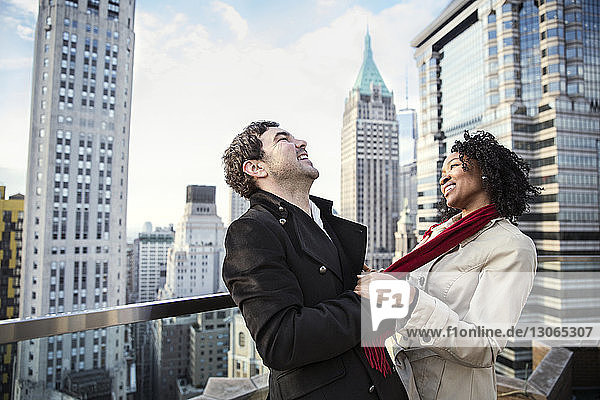 Cheerful couple standing on terrace with city buildings in background