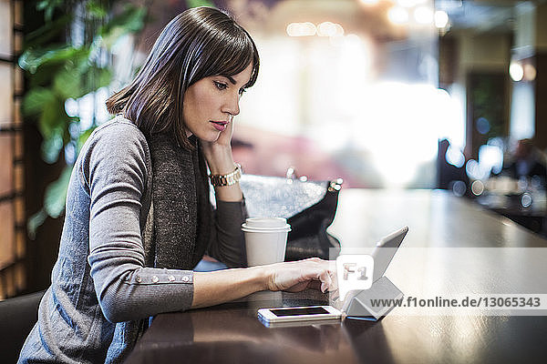 Woman looking at tablet computer while sitting in restaurant