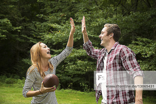 Couple high fiving while playing football in lawn