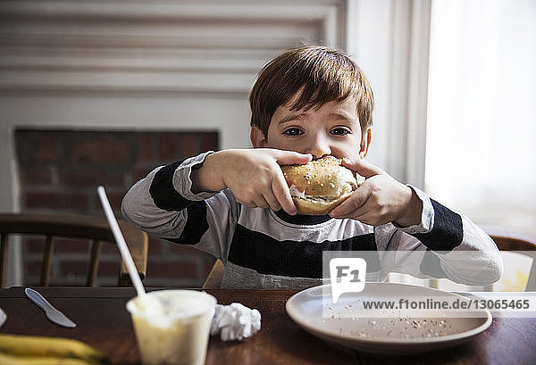 Porträt eines Jungen  der zu Hause einen Hamburger isst