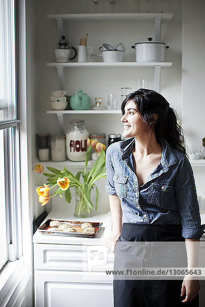 Nachdenkliche Frau schaut weg  während sie zu Hause an der Küchentheke steht