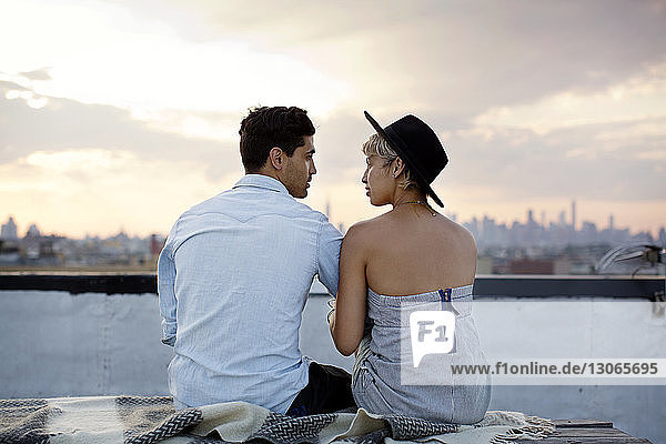 Rear view of couple talking while sitting on building terrace during sunset