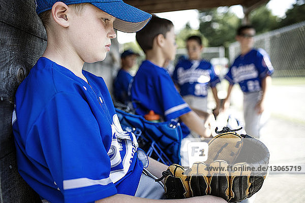 Thoughtful boy with sports glove sitting in dugout