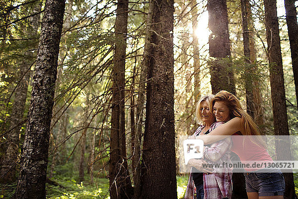 Happy mother and daughter embracing while standing amidst trees at forest
