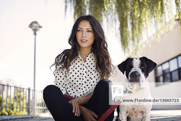 Frau sitzt mit Hund gegen Gebäude
