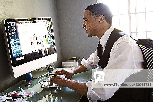 Seitenansicht eines Mannes  der am Desktop-Computer arbeitet  während er im Büro sitzt