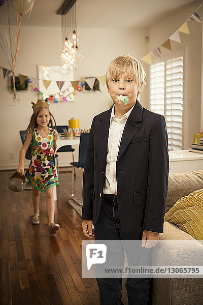 Portrait of boy standing with sister walking in background at home
