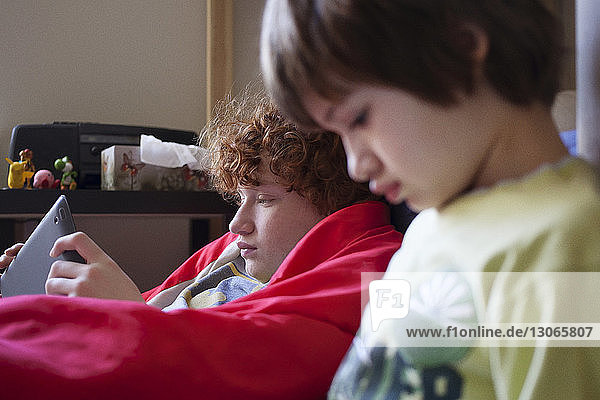 Junge benutzt Tablet-Computer  während er bei seinem Bruder zu Hause sitzt